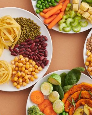A vibrant mix of legumes, vegetables, nuts, and pasta arranged on white plates showcasing a balanced, healthy diet.