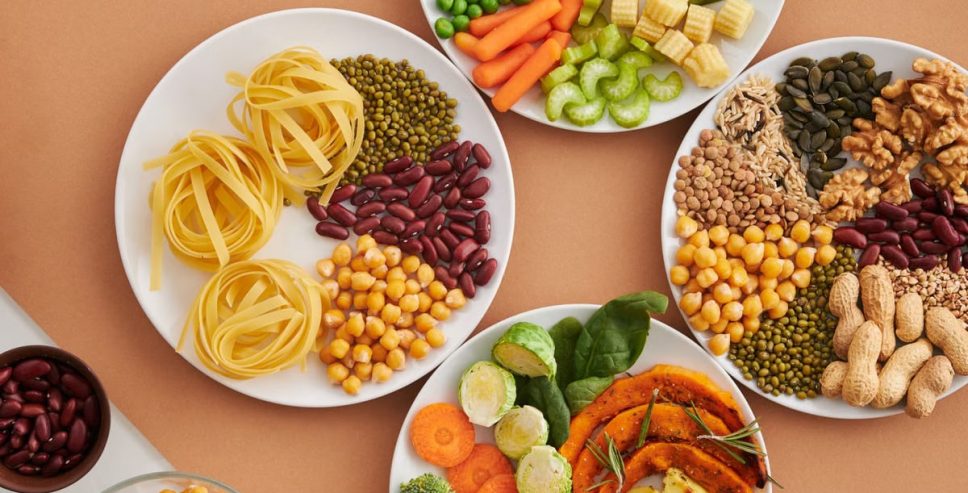 A vibrant mix of legumes, vegetables, nuts, and pasta arranged on white plates showcasing a balanced, healthy diet.