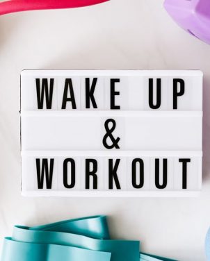 Top view closeup composition of wake up and workout inscription on light box surface among expanders and dumbbells and massage ball on white background